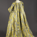 robe volante, vers 1730, lampas fond gros de Tours jaune citron broché soie verte, filé et frisé métalliques argent étincelant à décor stylisé de grenades, corbeille de fleurs et d’un kiosque d’inspiration chinoise inscrits entre les courbes et contre-courbes de feuilles dentelées recourbées.