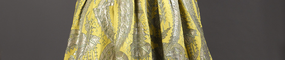 robe volante, vers 1730, lampas fond gros de Tours jaune citron broché soie verte, filé et frisé métalliques argent étincelant à décor stylisé de grenades, corbeille de fleurs et d’un kiosque d’inspiration chinoise inscrits entre les courbes et contre-courbes de feuilles dentelées recourbées.