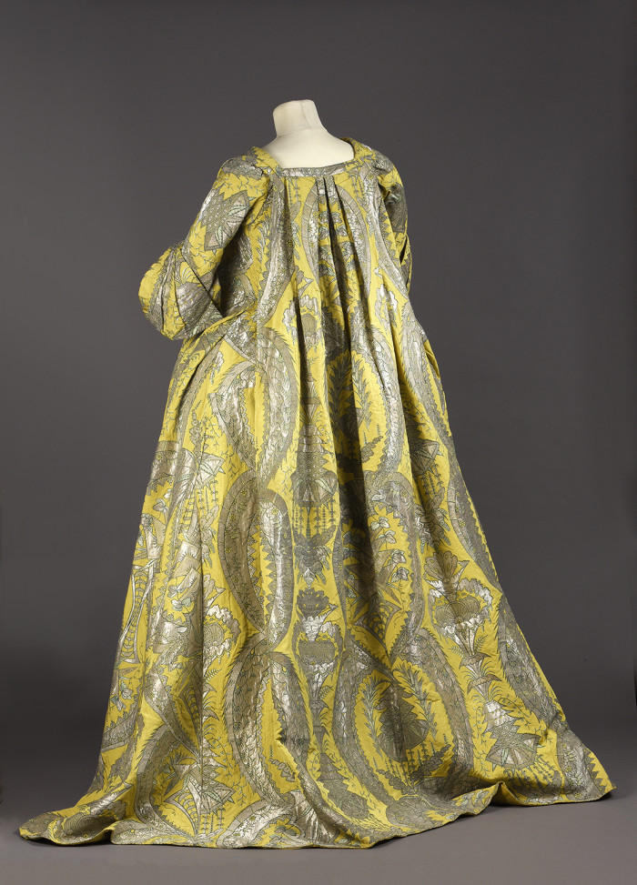 robe volante, vers 1730, lampas fond gros de Tours jaune citron broché soie verte, filé et frisé métalliques argent étincelant à décor stylisé de grenades, corbeille de fleurs et d’un kiosque d’inspiration chinoise inscrits entre les courbes et contre-courbes de feuilles dentelées recourbées.