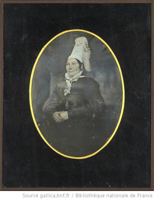 Portrait de femme, à mi-genoux, assise, de trois-quarts à gauche, les mains croisées, portant une coiffe normande, Gallica.bnf.fr