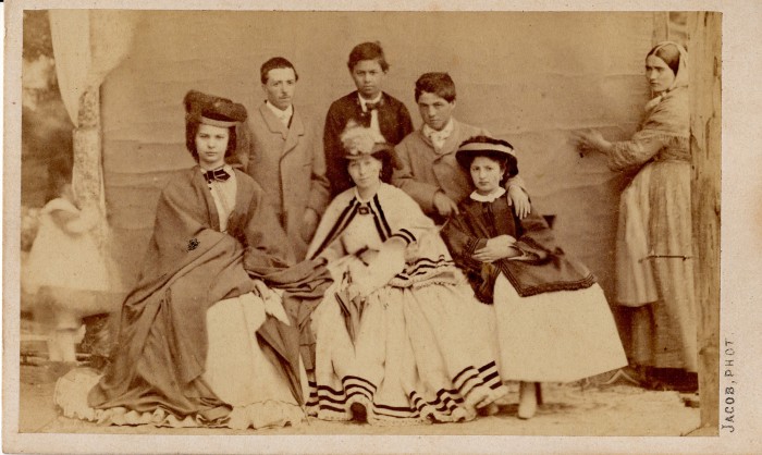 Portrait de groupe. De grands enfants posent en tenue hivernale d'extérieur, avec pour les filles cape, manteau ou immense châle. Sur le coté, tenant la tenture qui sert de fond, la servante est habillée de manière populaire. Photographie Jacob, Perpignan,vers 1850, collection particulière.