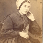 Portrait de jeune femme. C'est une jeune employée de maison portant une robe unie en drap de laine, un tablier et une cravate autour du cou. Sa coiffe est un simple « cofet » de calicot blanc amidonnée. Photographie Bidard frères, Perpignan, ver 1860, collection particulière.